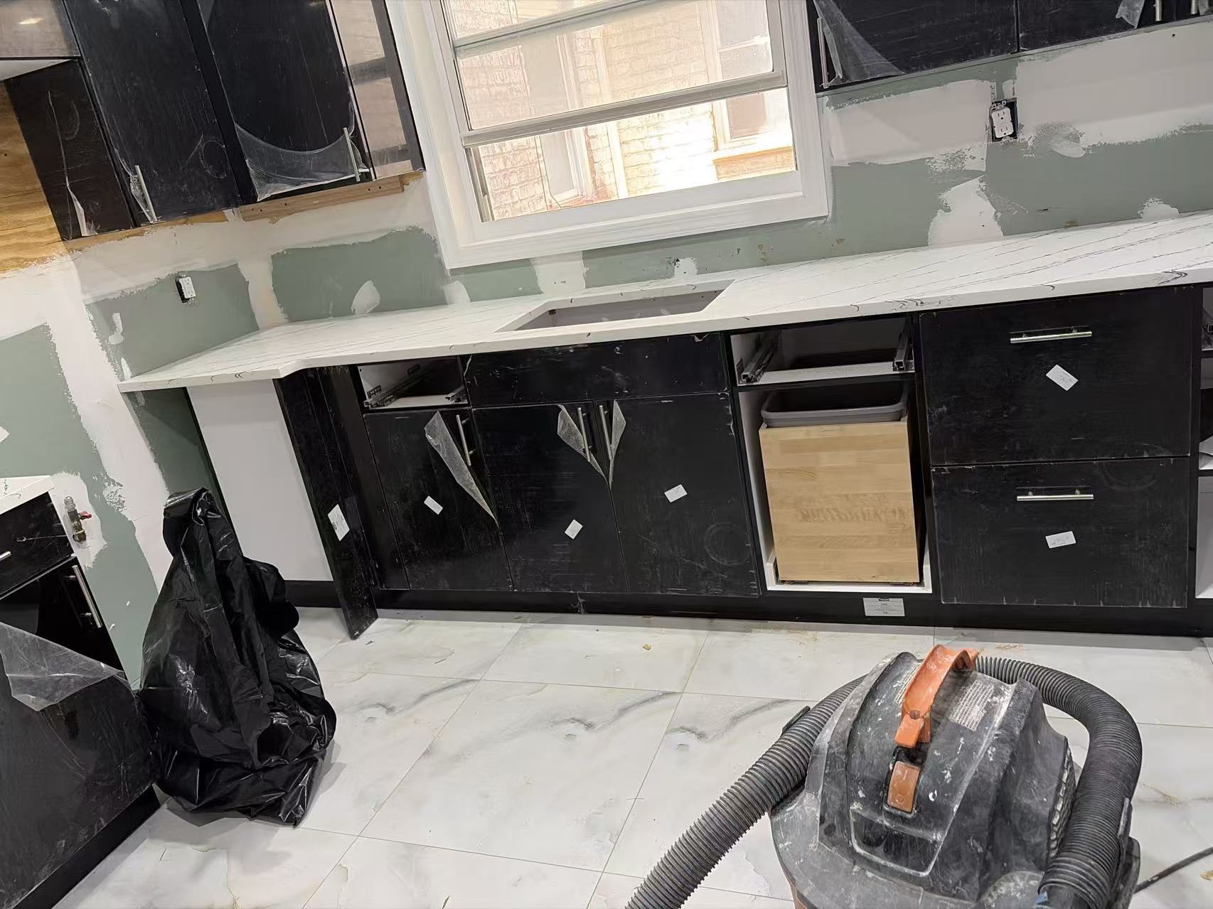 Sample 009G black flat-panel kitchen cabinets with white marble-look countertops during installation
