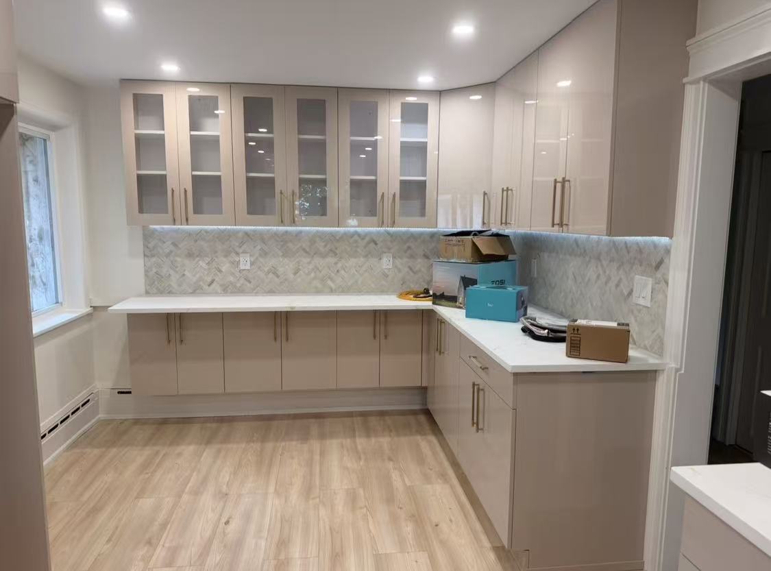 Sample 106G glossy taupe cabinetry with glass-front upper cabinets, brass pulls and white countertops