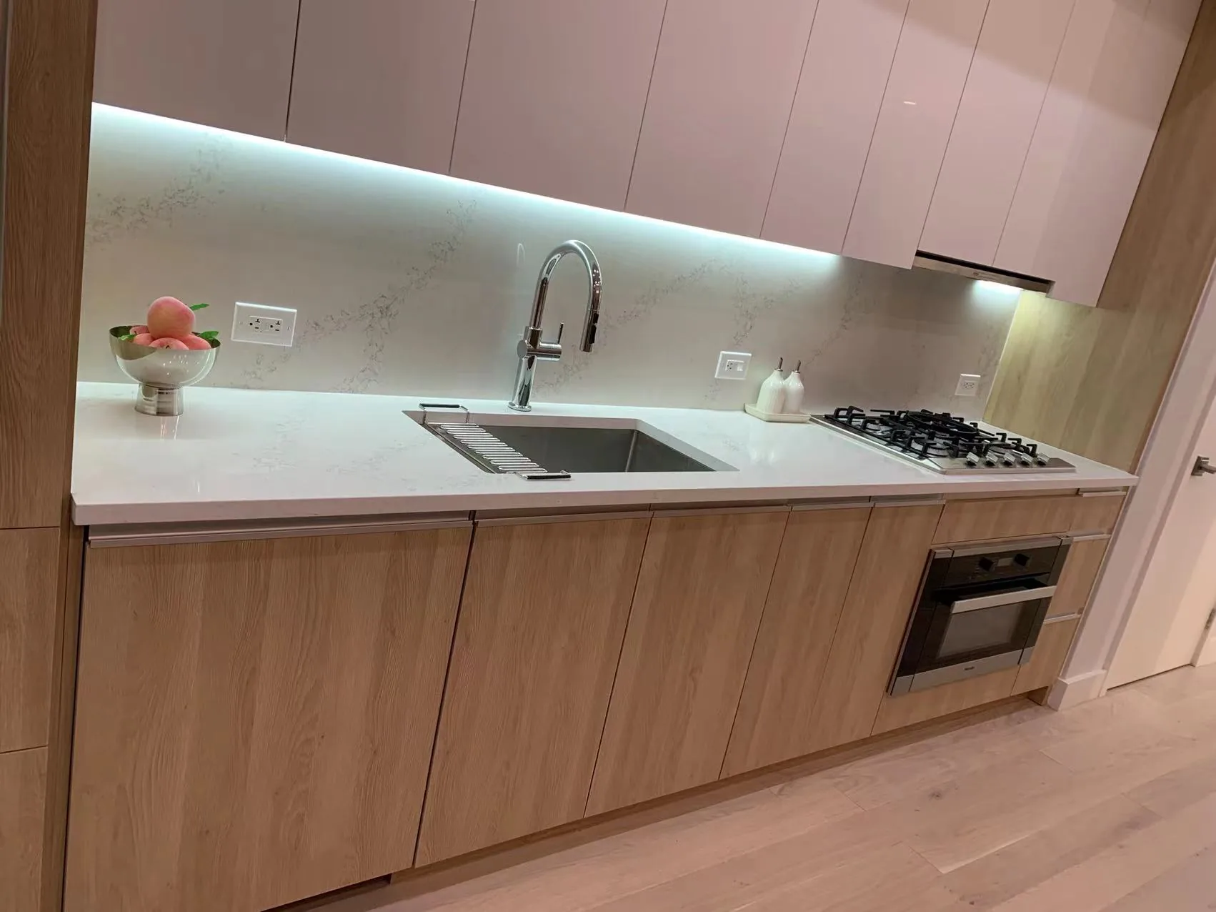 Compact light wood kitchen with glossy upper cabinets and under-cabinet lighting