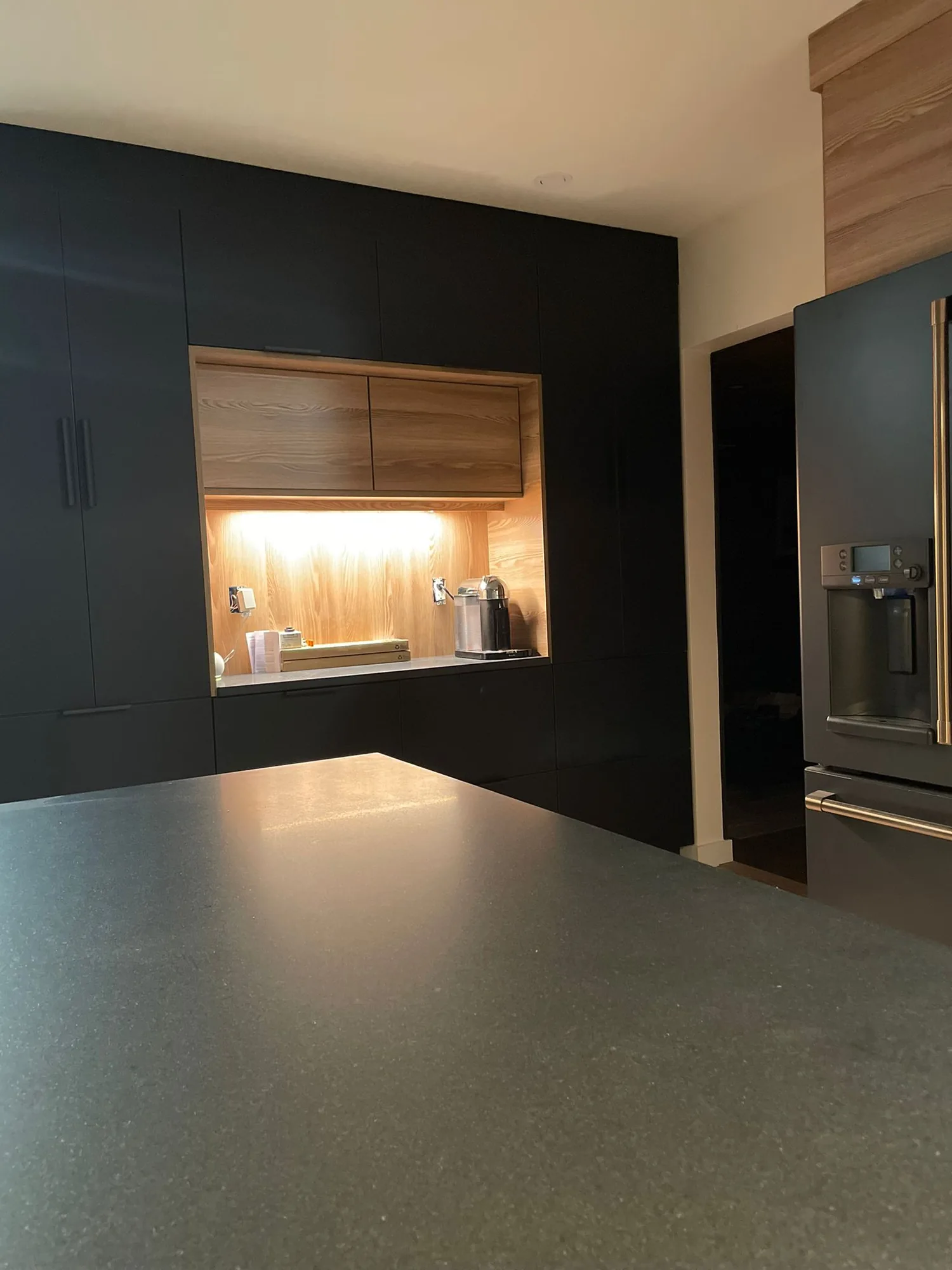 Matte black cabinetry with an illuminated wood coffee station