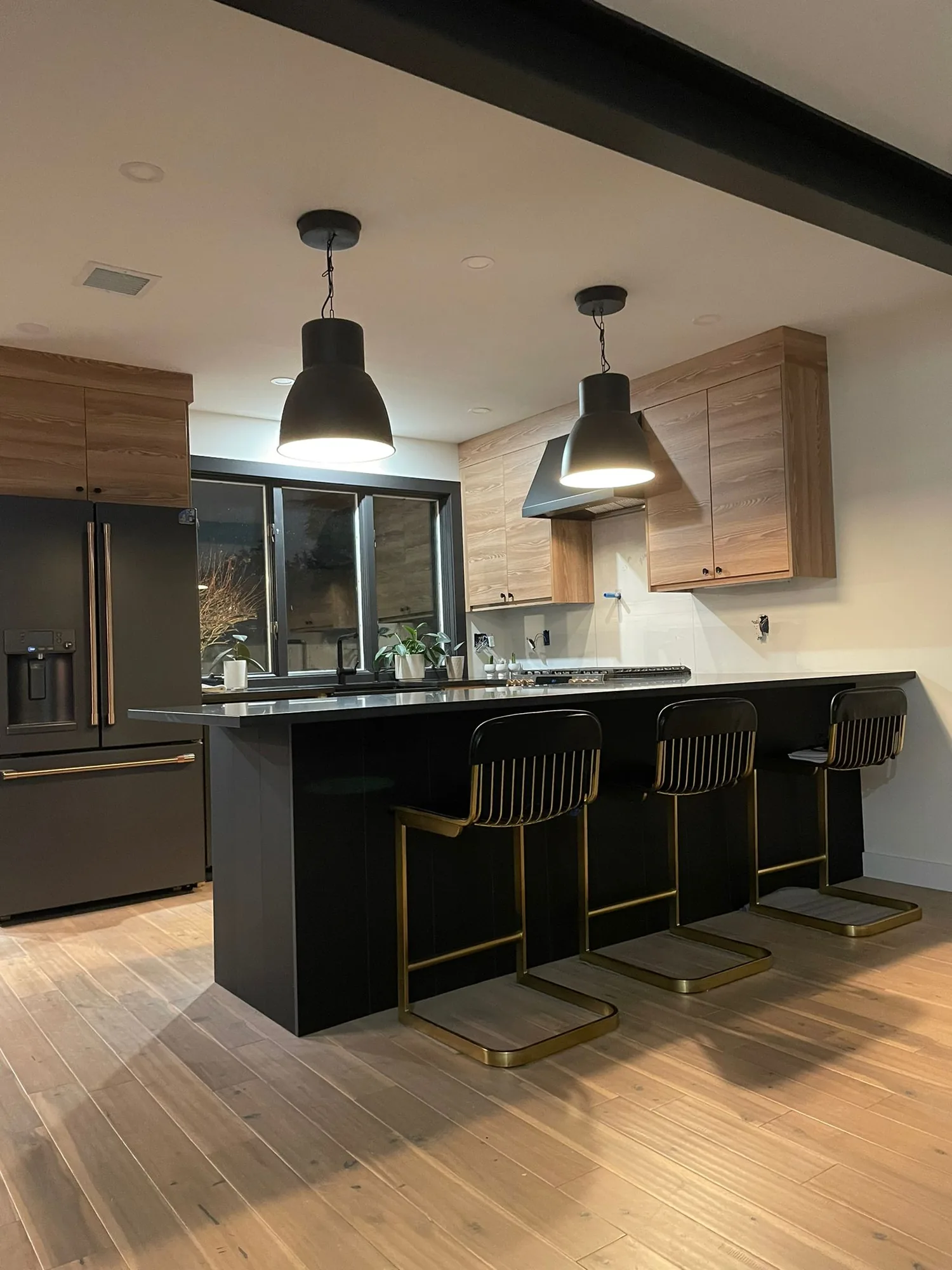 Black island kitchen with natural wood cabinets, pendant lights, and bar seating